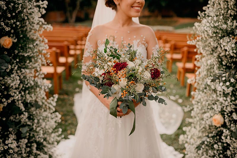 noiva em arco de flores com buquê na mão